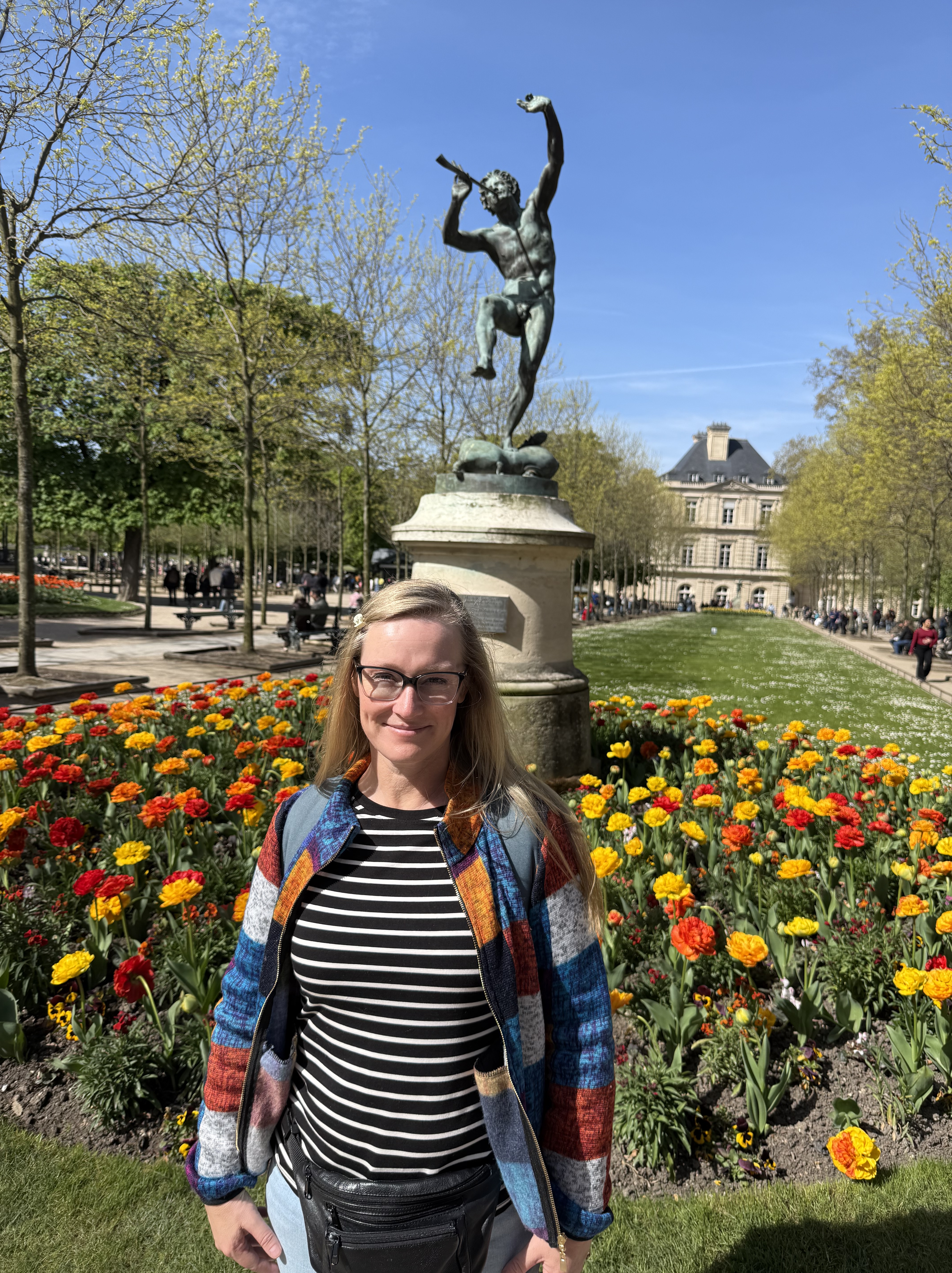 Picture of me with the Le Faune dansant sculpture in the background in a flowerbed of yellow and orange tulips