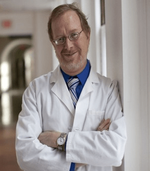Author image of Daniel J. Cox. He has a trimmed moustache and beard and wears glasses. He is wearing a white lab coat.