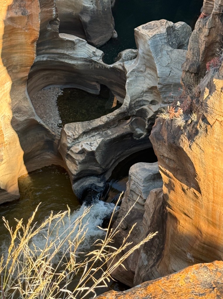 This is a close up of the pothole with the rapid gushing out of it and the surrounding golden cliffs.