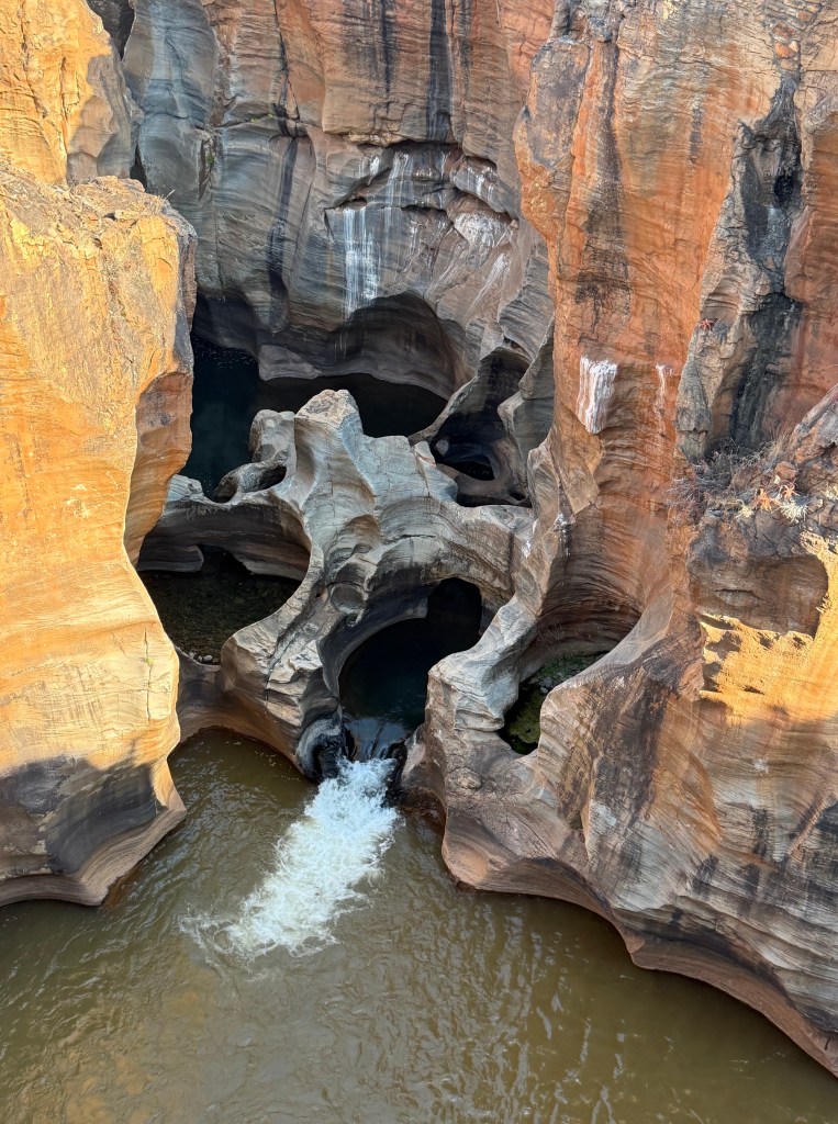 Close up of the potholes in the rock with a small rapid flowing from the centre pothole. The surrounding cliffs are bathed in golden light
